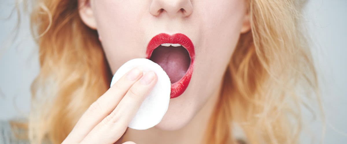 Frau schminkt sich roten Lippenstift ab.