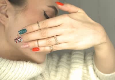 Manicure colorata in stile natalizio con anelli su dita e maglione bianco