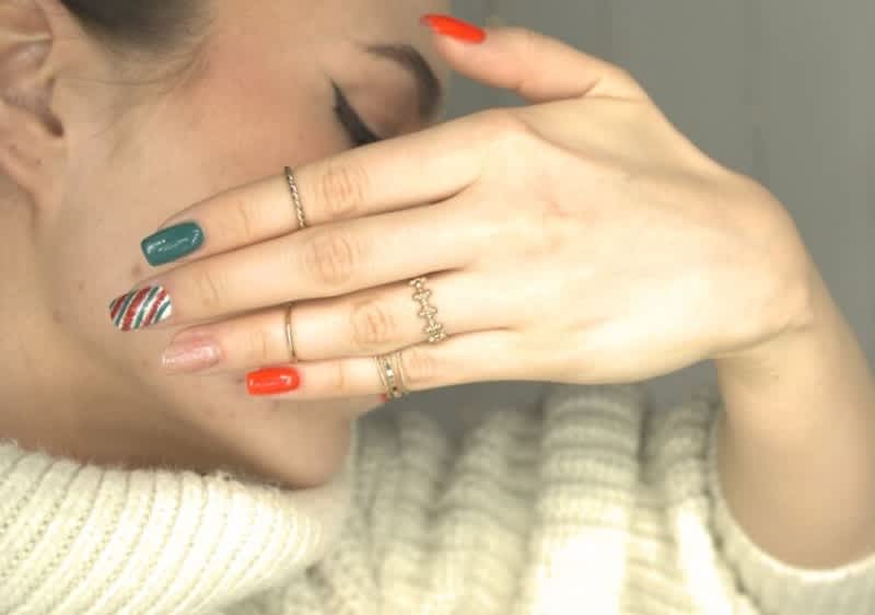 Manicure colorata in stile natalizio con anelli su dita e maglione bianco