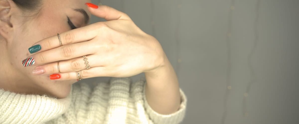 Manicure colorata in stile natalizio con anelli su dita e maglione bianco