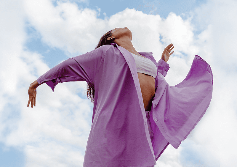 Ragazza in camicia viola balla con cielo e nuvole sullo sfondo