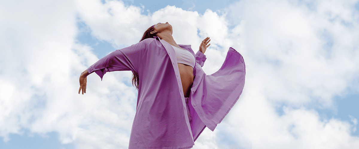 Ragazza in camicia viola balla con cielo e nuvole sullo sfondo