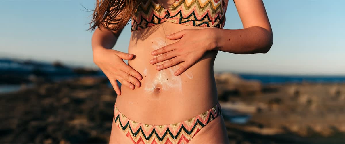 donna in costume con crema solare sulla pancia