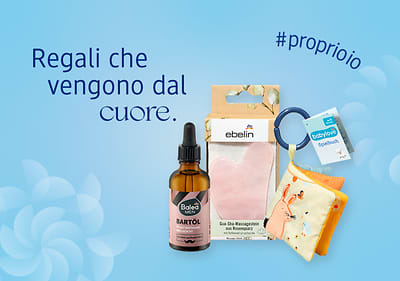 Regali di Natale con olio per la barba, pietra viso per massaggi Gua Sha e libro per bambini su sfondo azzurro con fiocchi di neve e frase Regali che vengono dal cuore.