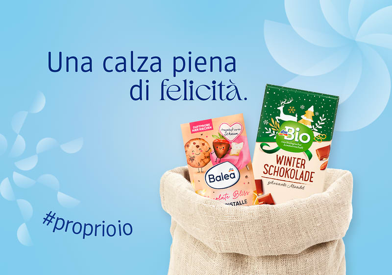 Calza della befana con sali da bagno Balea e tavoletta di cioccolato dmBio su sfondo azzurro con elementi astratti bianchi