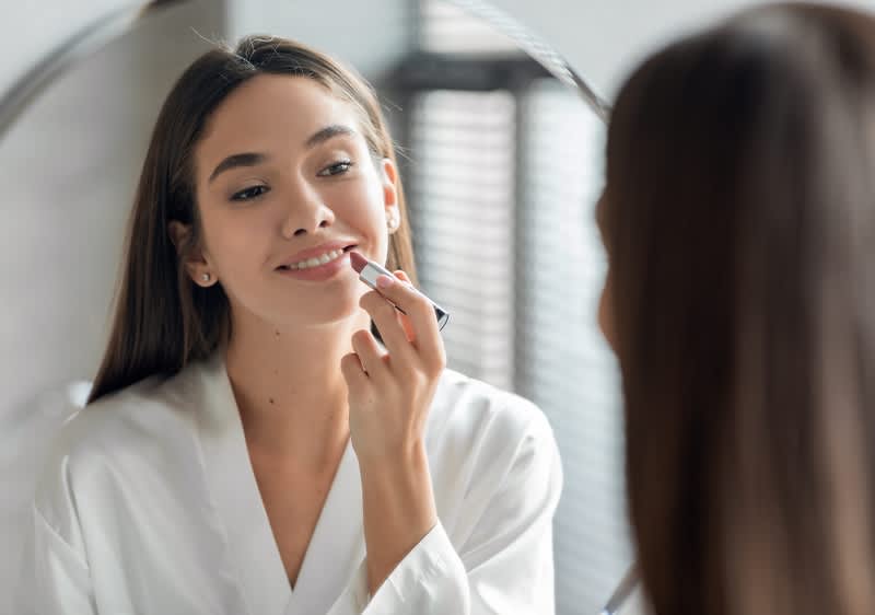Ragazza allo specchio che si trucca le labbra