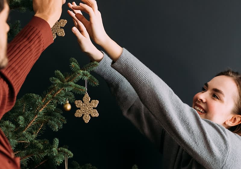 Una coppia decora l'albero di Natale con addobbi dorati