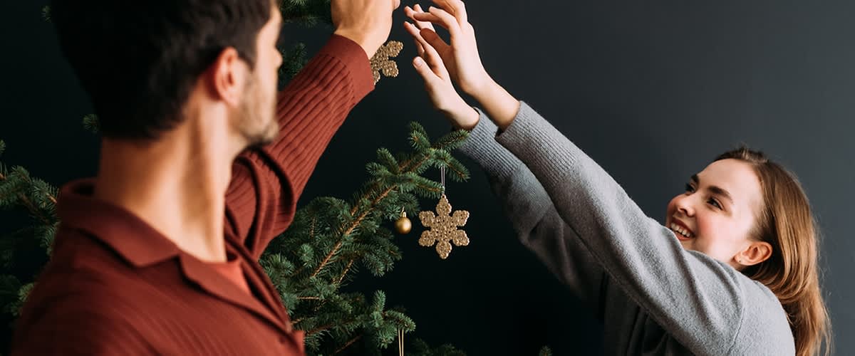 Una coppia decora l'albero di Natale con addobbi dorati