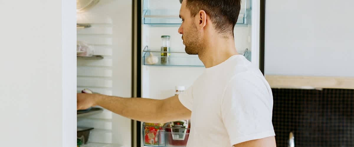 Uomo davanti al frigorifero aperto che prende cibo dai ripiani