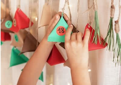 Calendario dell'avvento fai da te con scatole colorate appese al muro e mani di bambino che tengono la casella numero 18