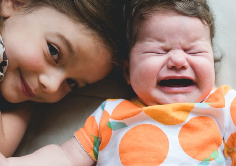 bambina sorridente sdraiata accanto a bebè che piange