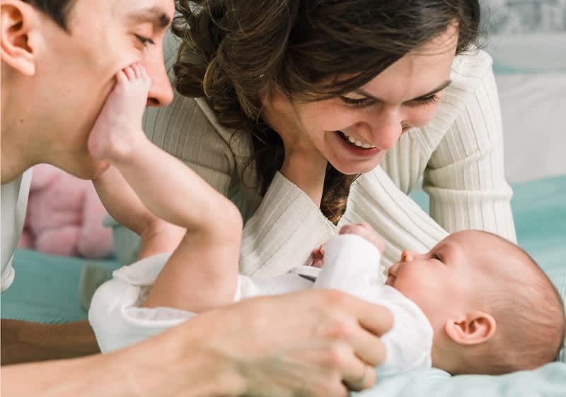 mamma e papà ridono con neonato