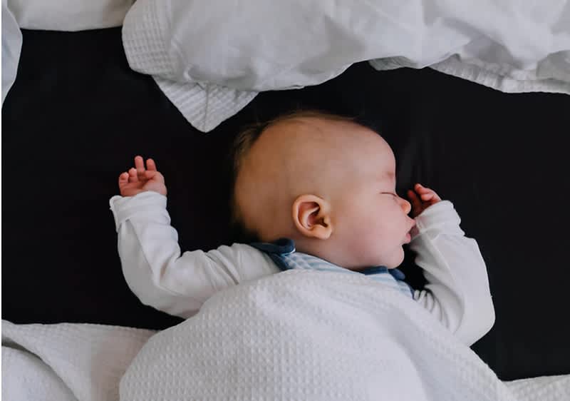 bebè dorme ben coperto sul letto