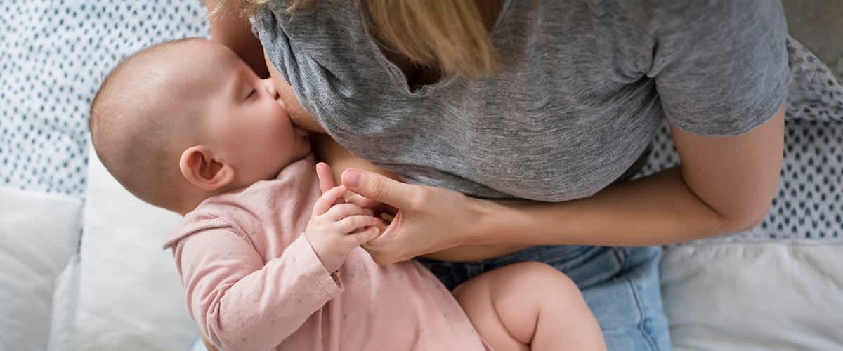 Madre che tiene in braccio e allatta un neonato con vestiti rosa