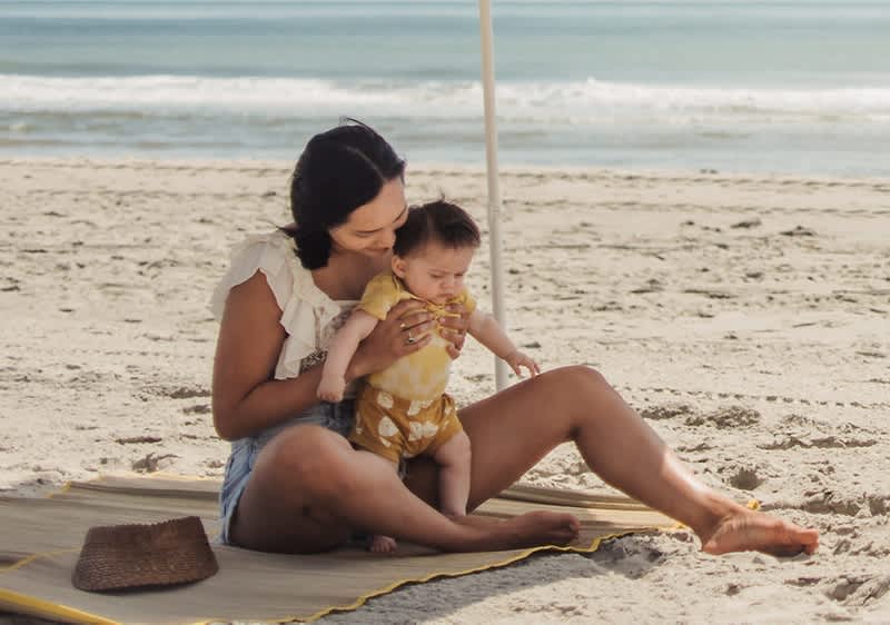 Madre e bambino seduti su una spiaggia con mare sullo sfondo
