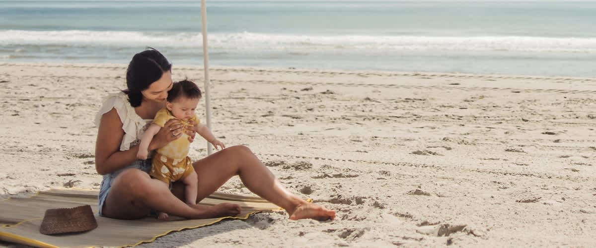 Madre e bambino seduti su una spiaggia con mare sullo sfondo