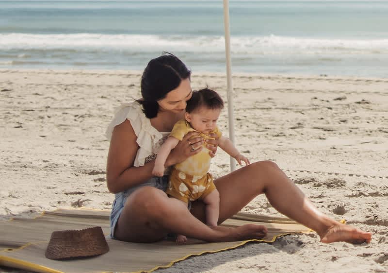Madre e bambino seduti su una spiaggia con mare sullo sfondo