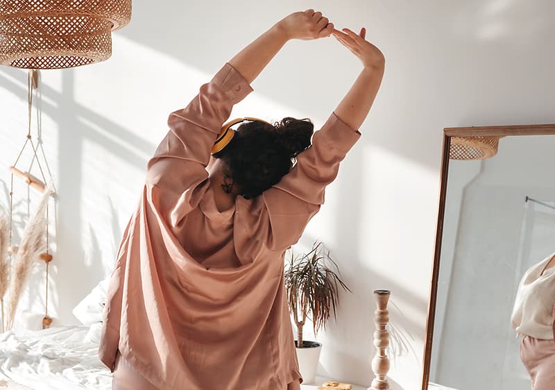 Donna che si allunga in una stanza luminosa con piante e specchio