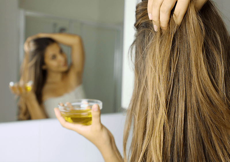 Donna applica olio d'oliva sui capelli davanti allo specchio