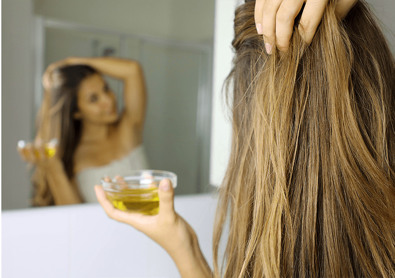 Donna applica olio d'oliva sui capelli davanti allo specchio