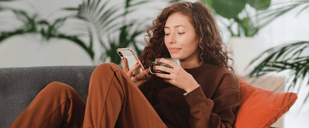 Donna con capelli ricci tiene smartphone e tazza