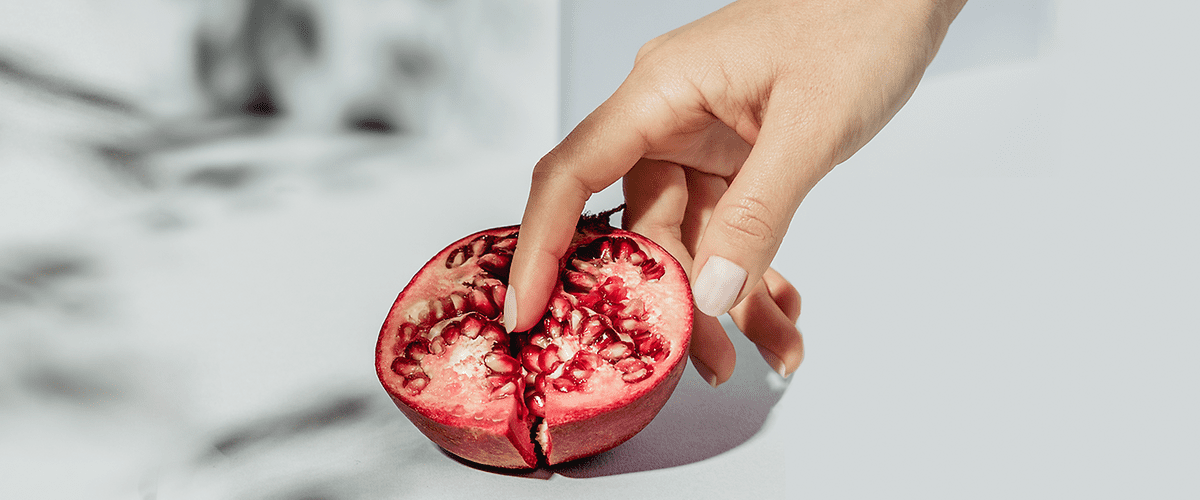 Mano che tiene una melagrana aperta su sfondo bianco