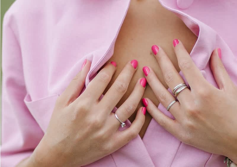 Unghie rosa e anelli su mani che aprono camicia rosa