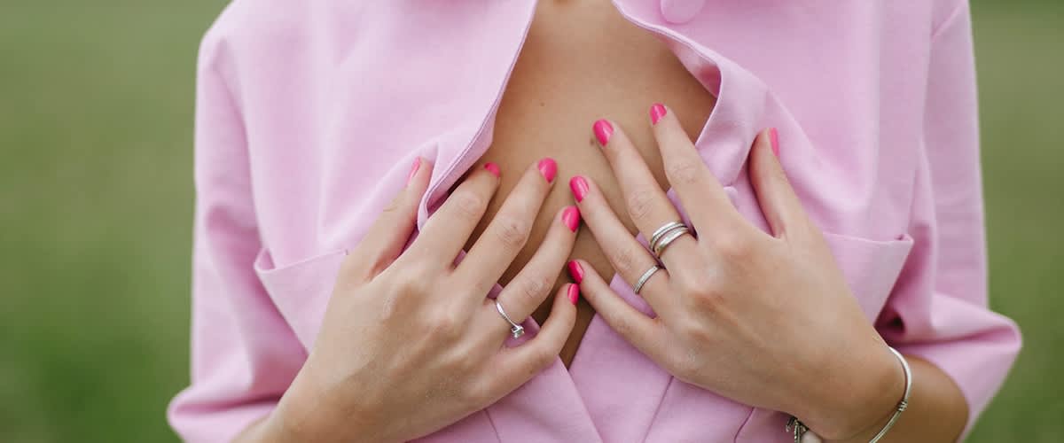 Unghie rosa e anelli su mani che aprono camicia rosa