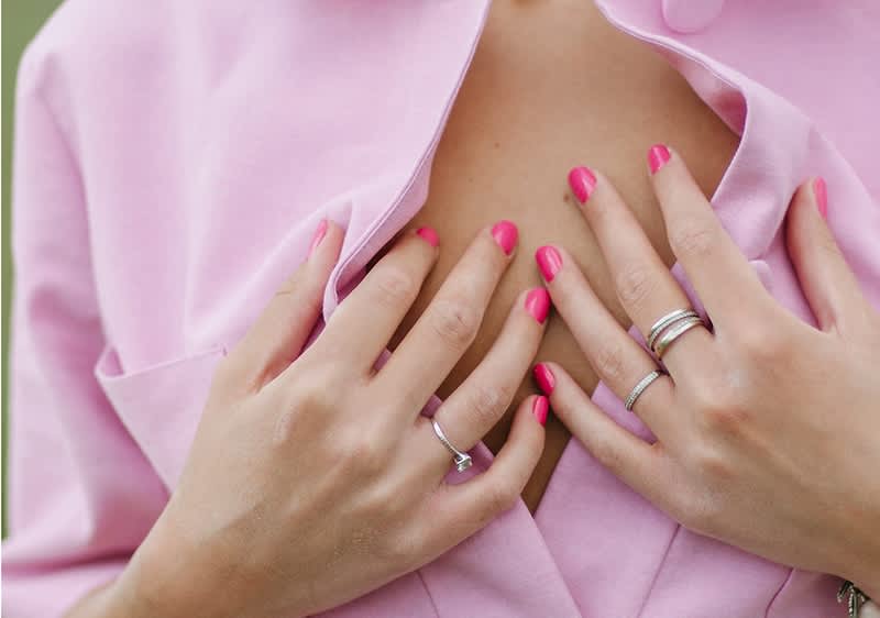 Unghie rosa e anelli su mani che aprono camicia rosa