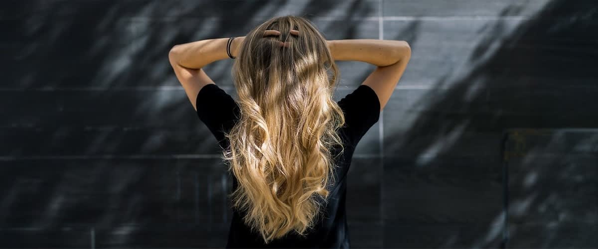 Capelli biondi mossi di donna di spalle con mani tra i capelli
