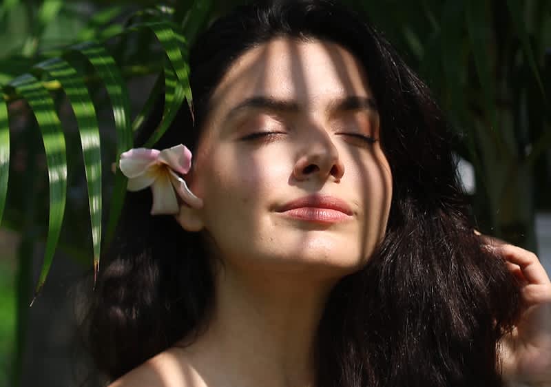 Donna con fiore bianco tra capelli scuri con foglie verdi sullo sfondo