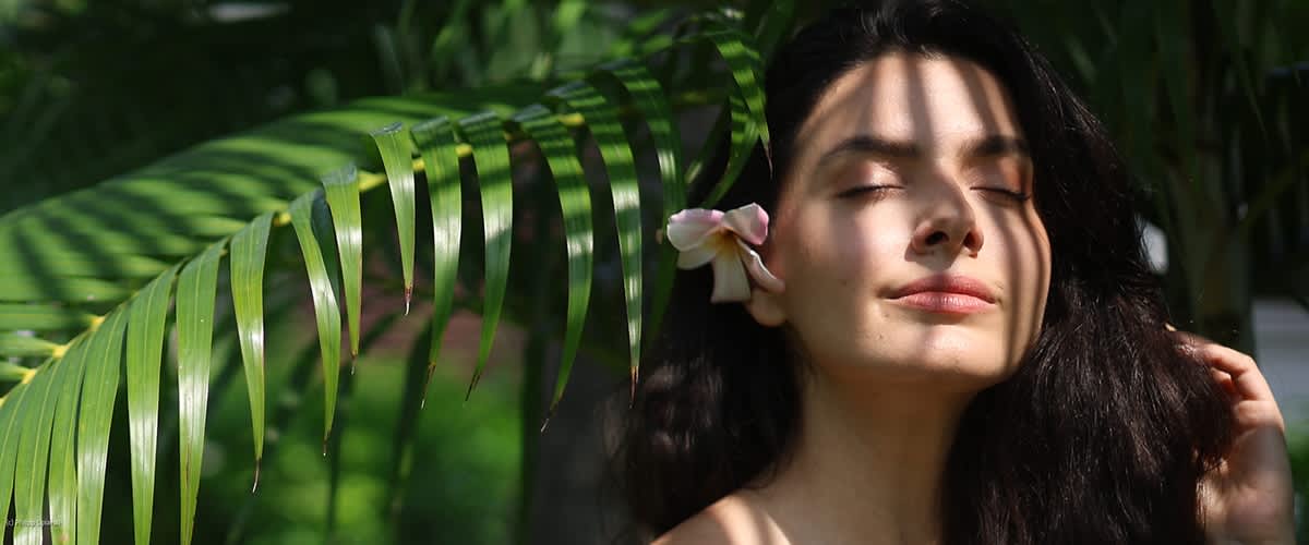Donna con fiore bianco tra capelli scuri con foglie verdi sullo sfondo
