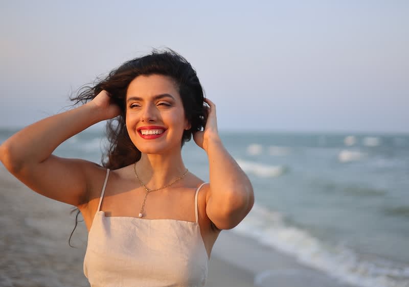 Donna in abito estivo sulla spiaggia con mare sullo sfondo