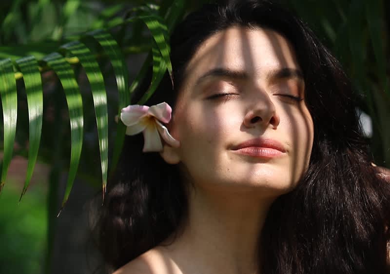 Donna con fiore tra i capelli sotto foglie verdi