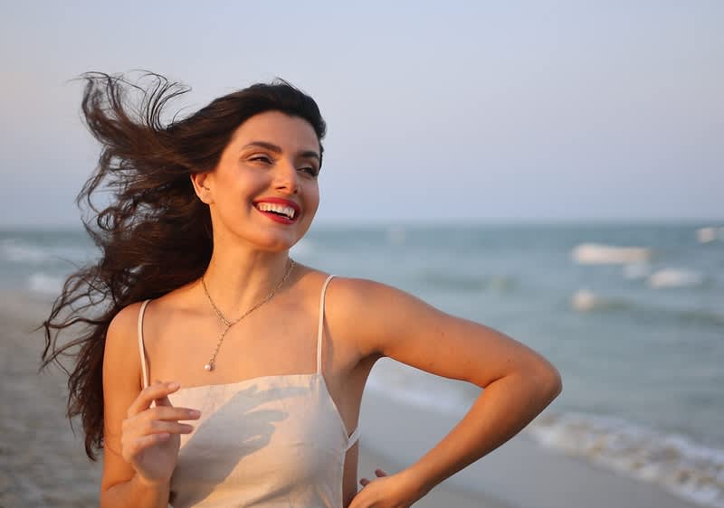 Donna con capelli mossi ride sulla spiaggia al tramonto