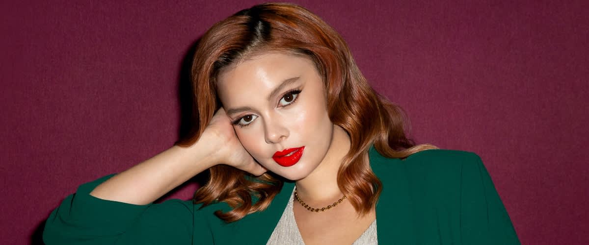 Donna con capelli ondulati castani e blazer verde su sfondo rosso