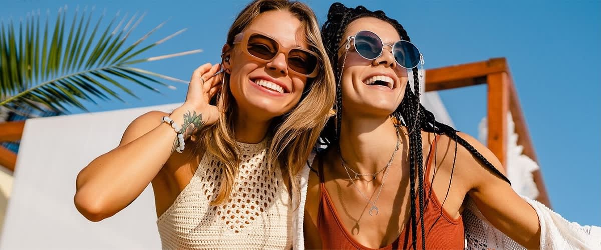 Due donne con abiti estivi e accessori alla moda ridono