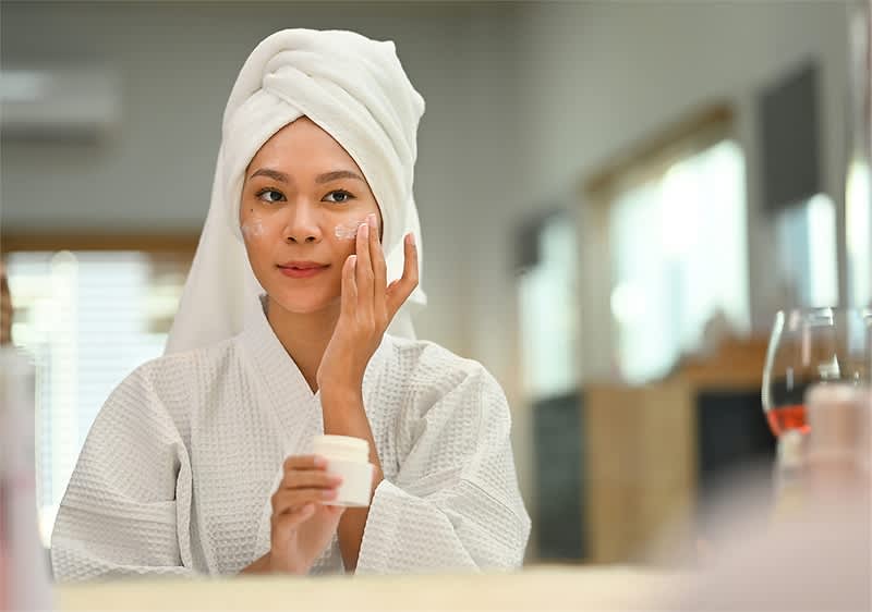 Donna in accappatoio si applica crema viso davanti allo specchio