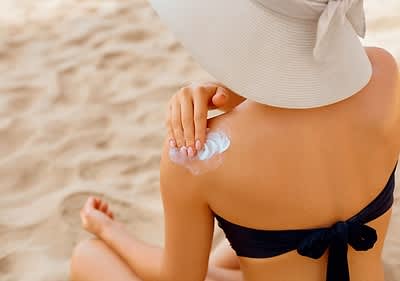 Donna in spiaggia applica crema solare sulla spalla