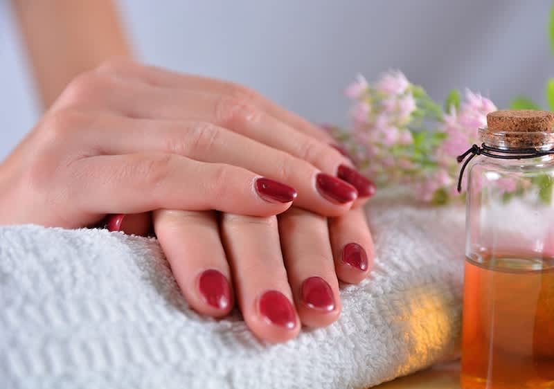 Manicure con smalto vegano rosso su mani appoggiate su asciugamano