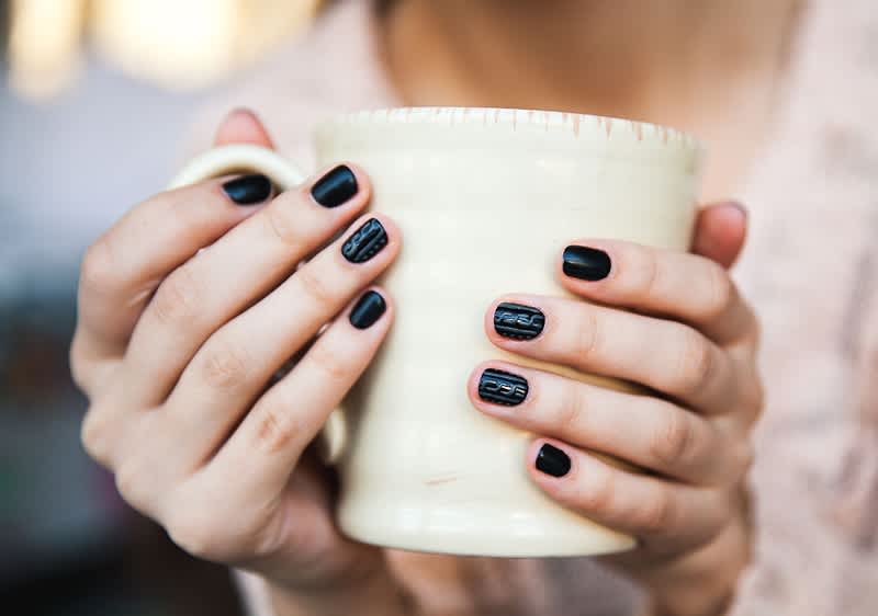 Manicure nera su mani che tengono una tazza