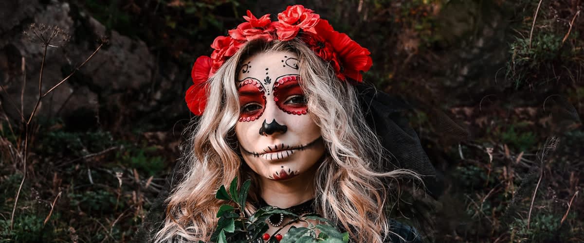 Ragazza bionda con trucco da teschio messicano e corona di fiori rossi tra i capelli