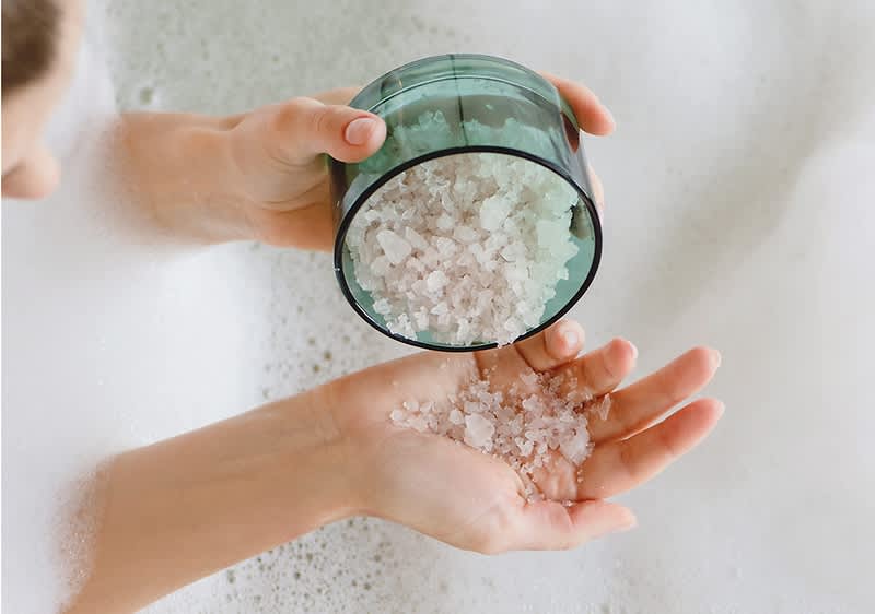 Sali da bagno versati in una mano sopra la schiuma di una vasca da bagno