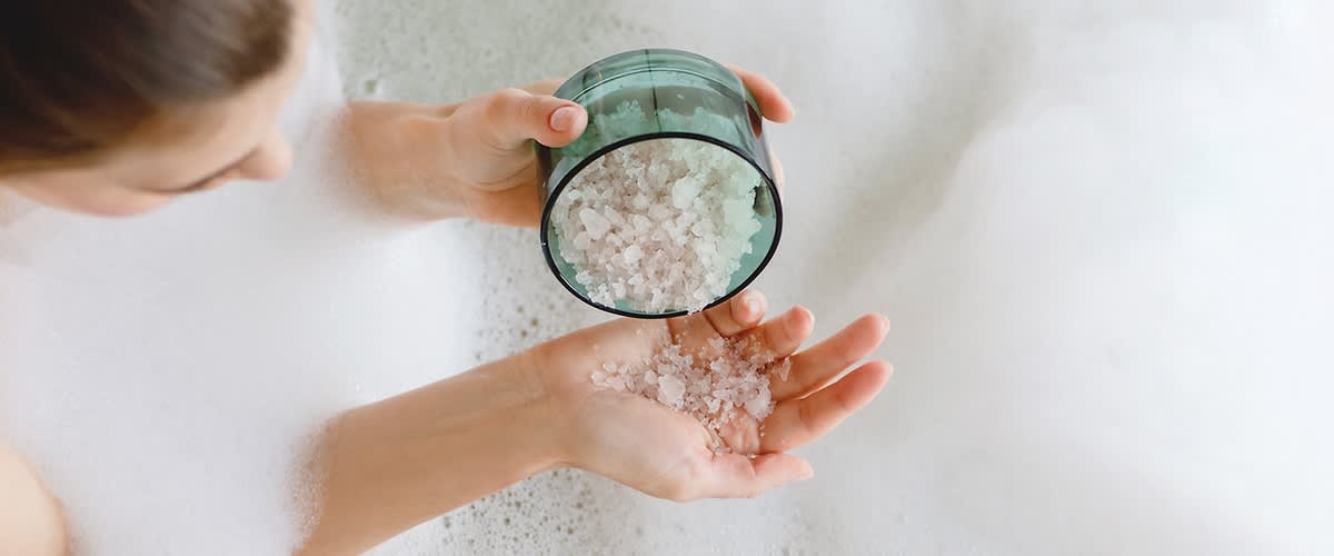 Sali da bagno versati in una mano sopra la schiuma di una vasca da bagno