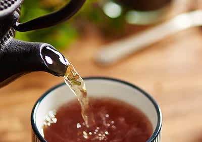 Tè nero versato con una teiera nera in una tazza bianca su un tavolo di legno