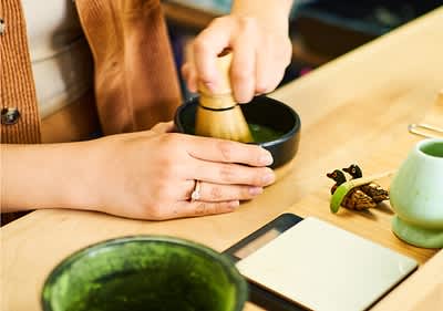 Preparazione del tè matcha con frusta di bambù in ciotola su tavolo di legno