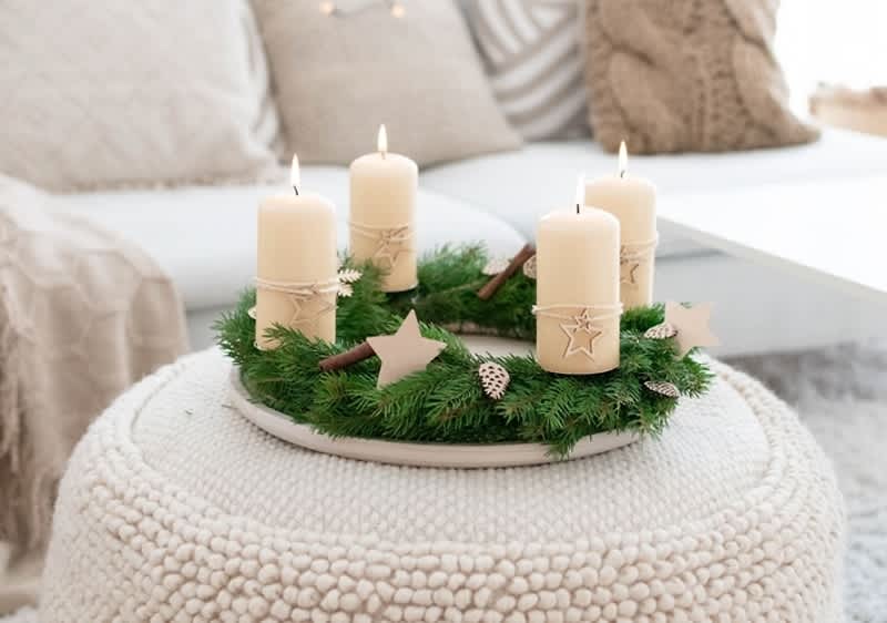 Corona dell'Avvento con candele bianche accese su tavolino in soggiorno accogliente