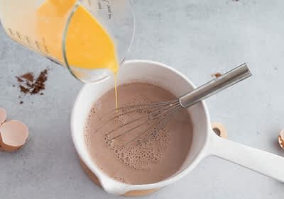 Preparazione di un composto al cioccolato con uova e frusta in una pentola bianca
