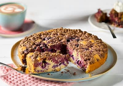 Torta di mirtilli con crumble su tavolo bianco con tazza di cappuccino in secondo piano