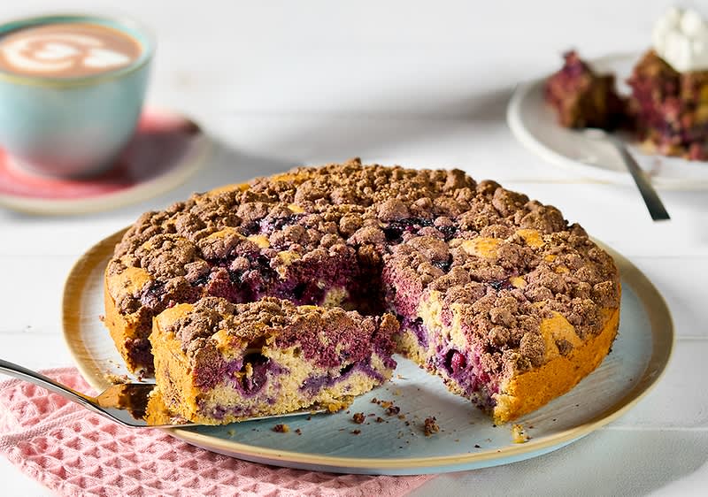 Torta di mirtilli con crumble su tavolo bianco con tazza di cappuccino in secondo piano